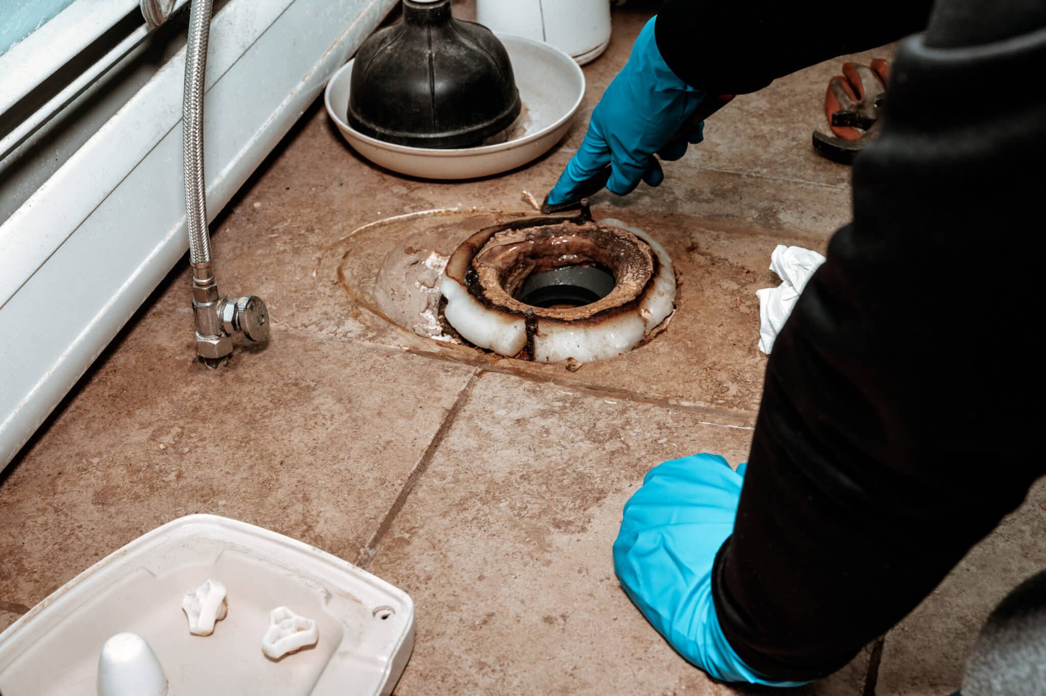 Close-up of a plumber replacing the wax ring seal at the base of a loose toilet.