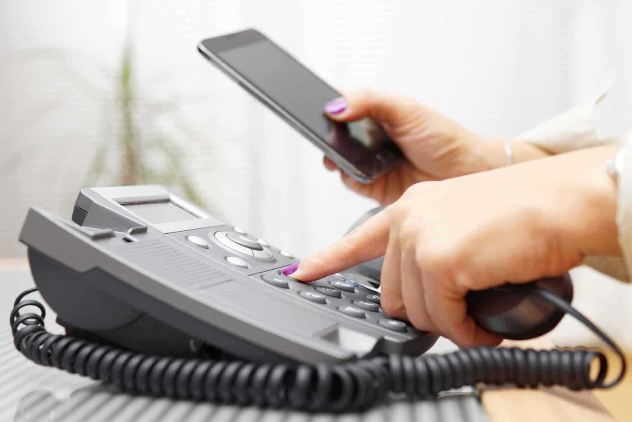A woman dialing a phone while looking at her smartphone, calling a professional for hot water recirculation system service.