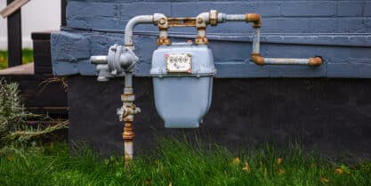 Old and rusted natural gas meter and pipeline system on a brick house, showing signs your home may need gas line replacement.