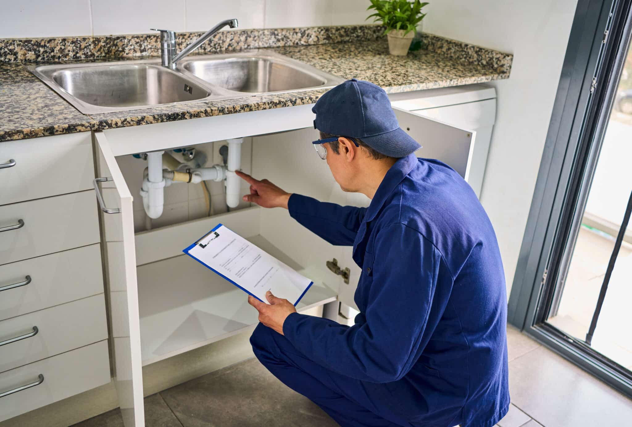 Plumber examining a kitchen plumbing system with a dishwasher air gap designed to prevent contaminated water from flowing back into the dishwasher.
